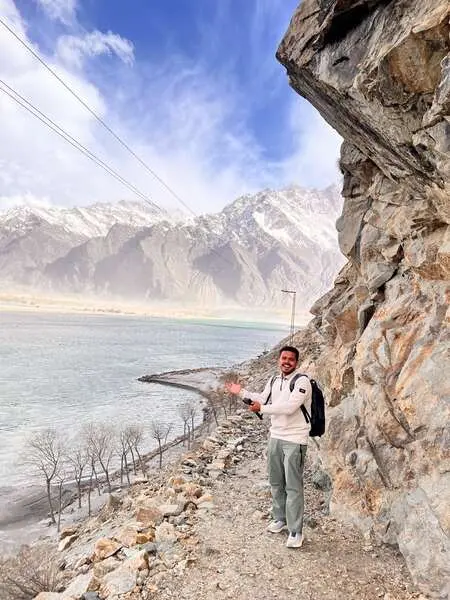 Saif on a mountain road above a lake with snow peaks behind