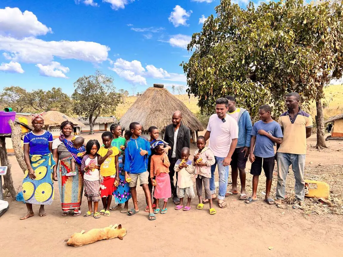 Saif with a large group of villagers outside thatched homes